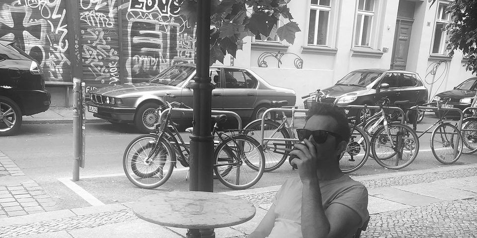 Some serious guy in sunglasses drinking coffee on a street in Berlin, thinking about music production.
